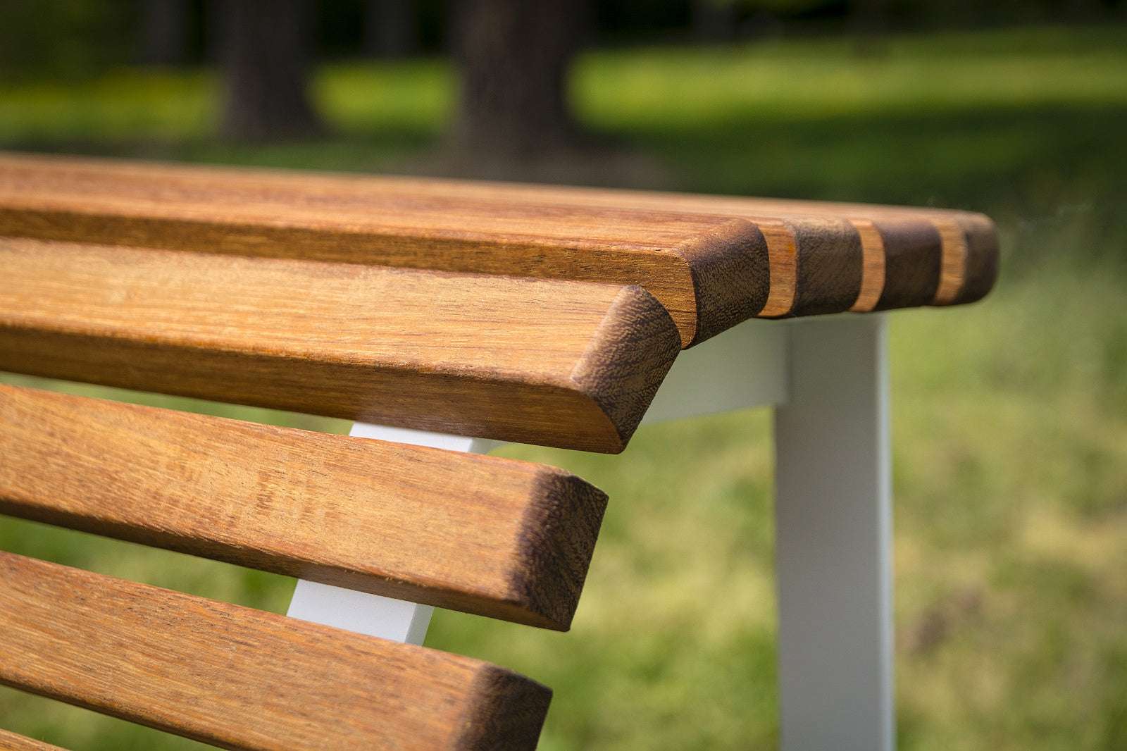Holzparkbank mit weißen Metallbeinen, platziert auf einer grünen Rasenfläche im Freien.