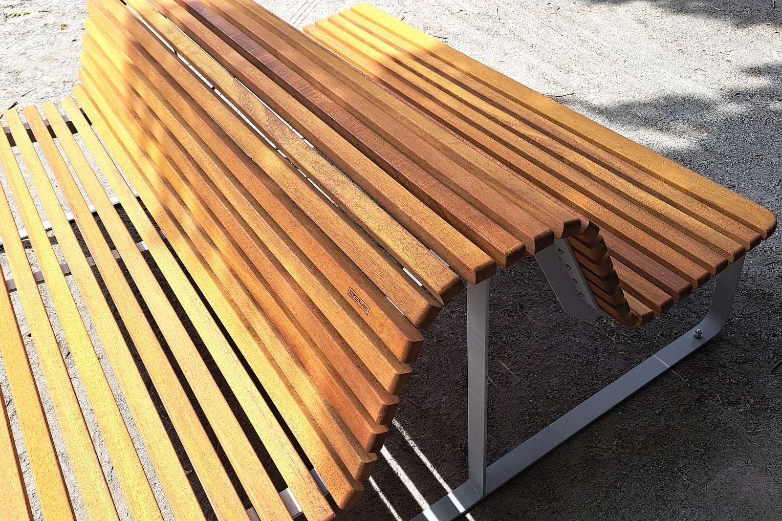 Moderne Holzparkbank mit Metallrahmen auf einem Kiesweg, stilvolles Design für Außenbereiche.