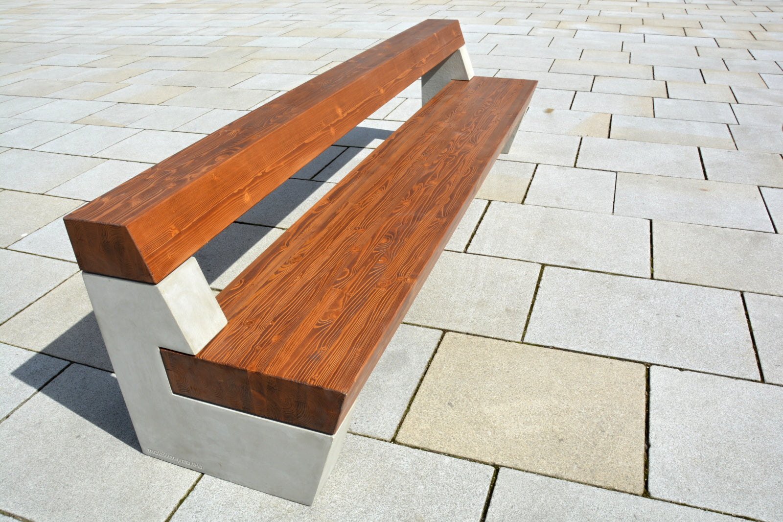 Eine moderne Bank aus Holz und Beton steht auf einem gepflasterten Platz, mit klaren Linien und ansprechendem Design.