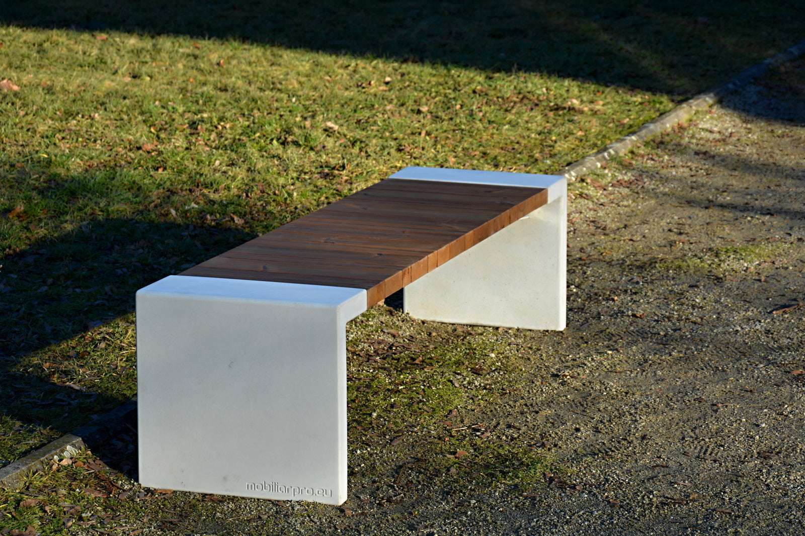 Moderne Bank mit Holzsitzfläche und Betonfüßen auf einem Kies- und Grasuntergrund im Freien.