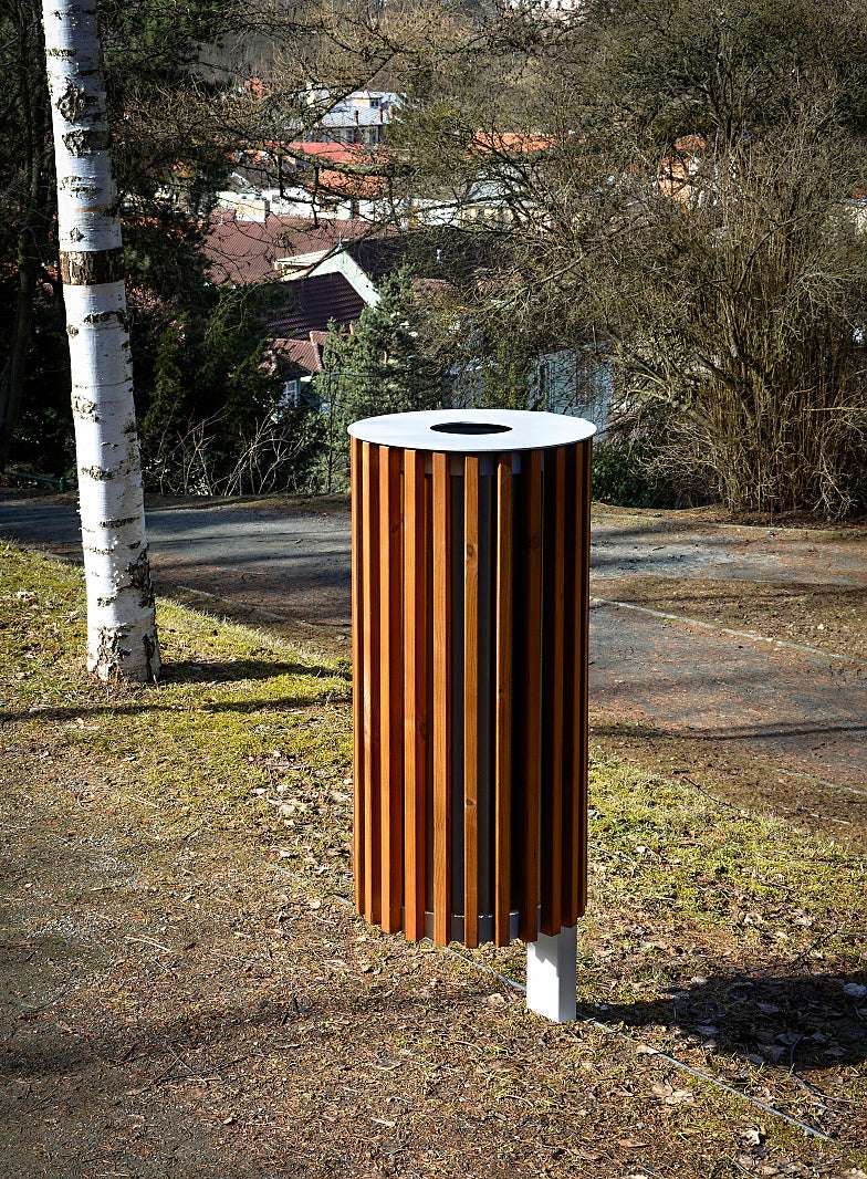 Moderner, freistehender ZET Abfallbehälter aus Holzlamellen auf Gehweg mit Bäumen und Häusern im Hintergrund.