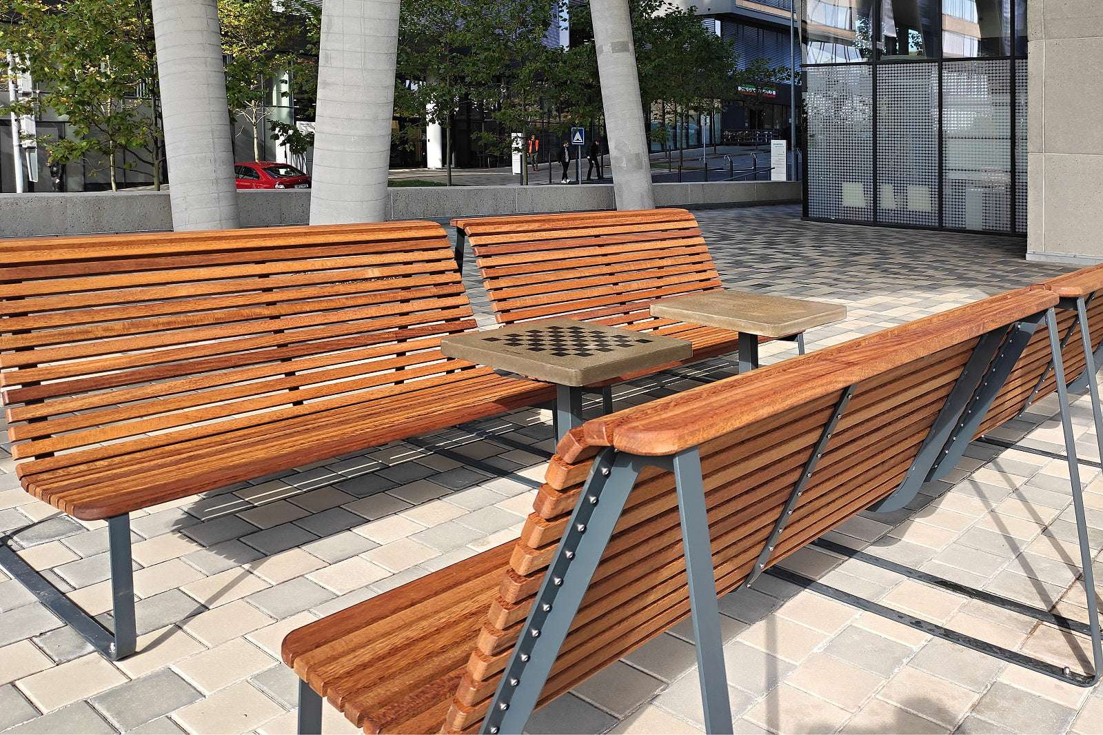 Holz-Sitzbänke im Freien mit eingebautem Schachbrett-Tisch auf gepflastertem Platz.