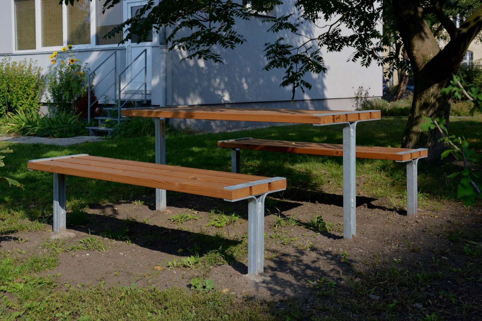 Drei Holzbänke und ein Tisch auf Metallgestell im Freien unter einem Baum.