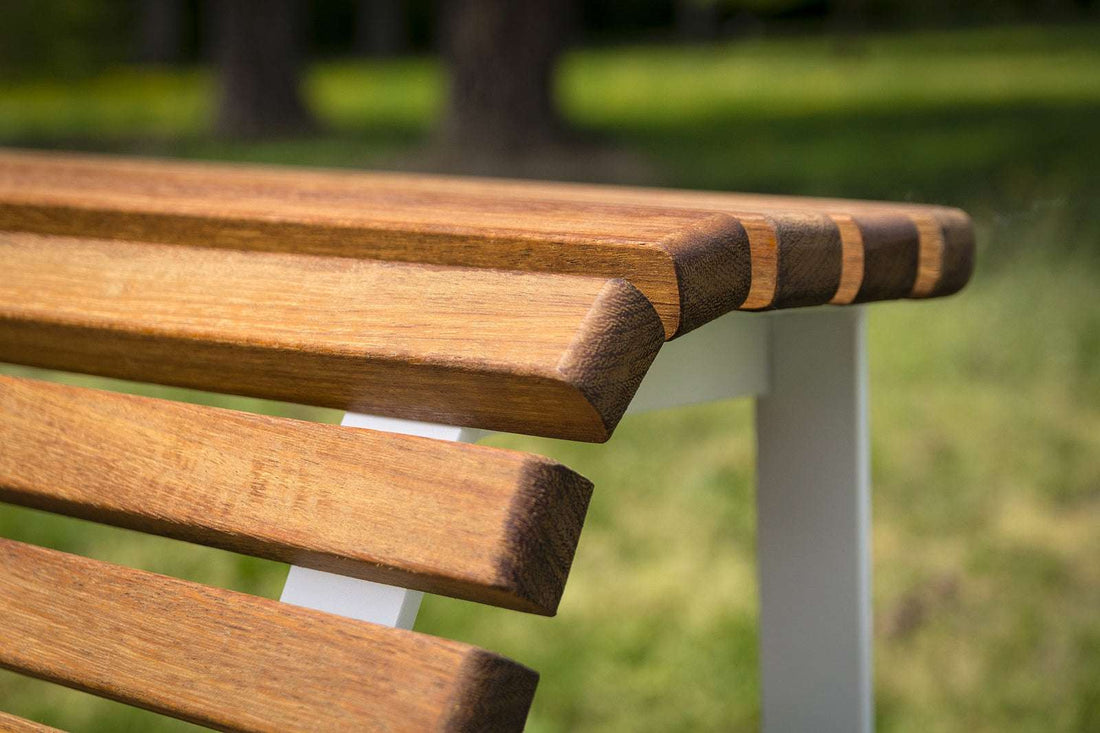 Holzparkbank mit weißen Metallbeinen, platziert auf einer grünen Rasenfläche im Freien.