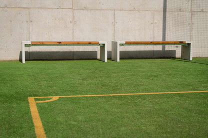 Zwei moderne Bänke auf Kunstrasen vor einer Betonwand, ideal für Außenbereiche und Sportplätze.