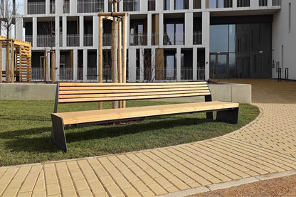 Moderne Holzbank mit Metallgestell auf gepflastertem Weg vor einem Gebäude mit Glasfassade.