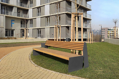 Moderne Holzbank auf einem gepflasterten Weg in einem städtischen Park vor einem Wohngebäude.