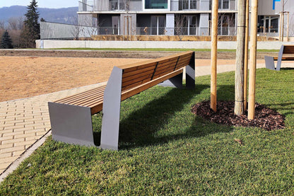 Moderne Holzbank auf Rasen neben gepflastertem Gehweg vor einem Gebäude im Freien platziert.