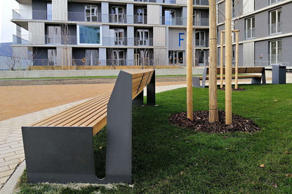 Moderne Holzbänke mit Metallrahmen auf einem begrünten Platz vor einem Wohngebäude.