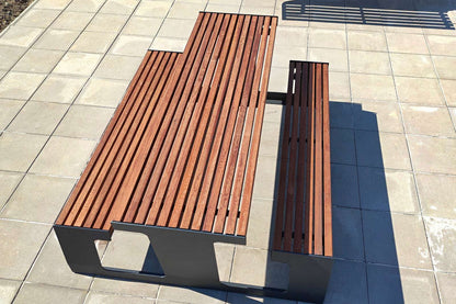 Moderne Gartenbank aus Holz und Metall auf gepflastertem Boden bei Sonnenschein.
